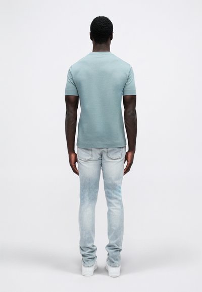 Svijetloplava majica s kratkim rukavima, mješavina pamuka, uparena s izblijedjelim svijetloplavim trapericama i bijelim tenisicama; prikazano sa stražnje strane.