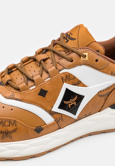 Baskets en cuir marron avec accents blancs, surface texturée, logo noir et motifs décoratifs. Comprend des lacets marron et une semelle en caoutchouc.