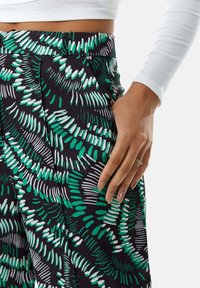Black pants with a leafy green and white pattern, featuring a relaxed fit, side pockets, and a flat waistband. Textured fabric adds dimension.