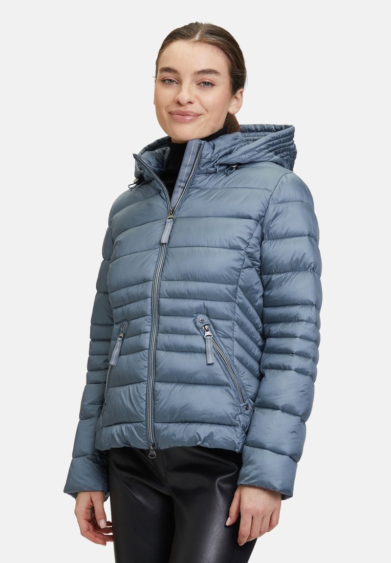 Vadderad blå jacka med dragkedja framtill, huva och sidofickor; har ribbad textur och en figursydd design.