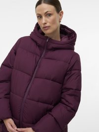 Sügavlilla puffer-jope, millel on kõrge krae, täis tõmblukk ja õmmeldud paneelid. Materjal on pehme ja veidi läikiv.