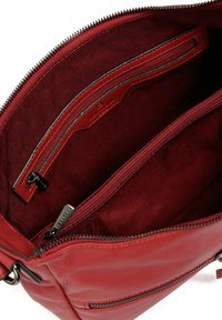 Interno di una borsa a tracolla in pelle rossa con una tasca con zip, foderatura in tessuto testurizzato e dettagli della cerniera in contrasto. Design spazioso e bordi puliti.