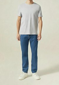 Šedé bavlněné tričko a modré džínové kalhoty. Tričko má kulatý výstřih a kalhoty mají rovné nohavice. Bílé tenisky.