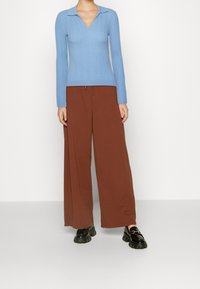 Haut à manches longues côtelé bleu clair avec un col en V, associé à un pantalon large marron et des mocassins noirs en cuir laqué à semelles épaisses.
