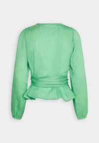 Haut vert en tissu froissé avec manches longues, taille peplum et détail noué dans le dos. Texture lisse avec une silhouette fluide.