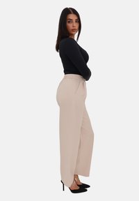 Pantaloni beige a gamba larga con una trama liscia, caratterizzati da una vestibilità comoda e una vita elasticizzata, abbinati a un top aderente nero a maniche lunghe.