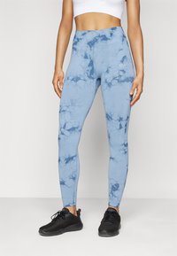 Leggings blu chiaro con un motivo marmorizzato, vita alta e tessuto texturizzato. Abbinati a scarpe da ginnastica nere.