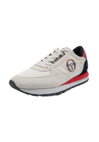 Athletic sneaker with a beige mesh and suede upper. Features red and navy accents, textured sole, and a circular logo applied on the side.