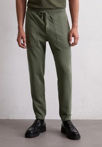 Olijfgroene joggerbroek van zacht materiaal, met een trekkoord taille, twee voorkruiszakken en geborduurd logo op de dij.