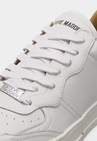 Baskets en cuir blanc avec lacets blancs, étiquette métallique "Steve Madden" sur le lacet, et "Steve Madden" imprimé sur la languette.