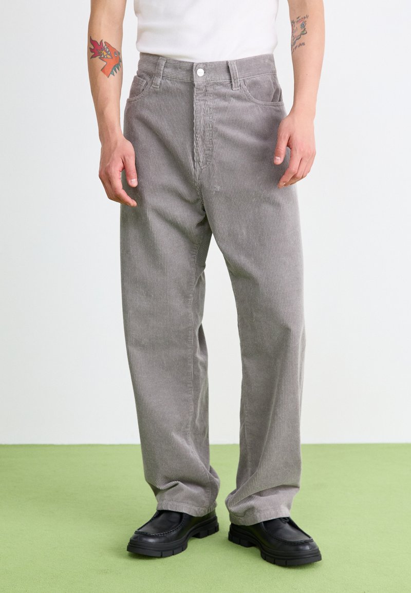 Pantalones de pana grises con un corte relajado, que cuentan con acanalado vertical, dos bolsillos frontales y un cierre de botón, combinados con zapatos negros.