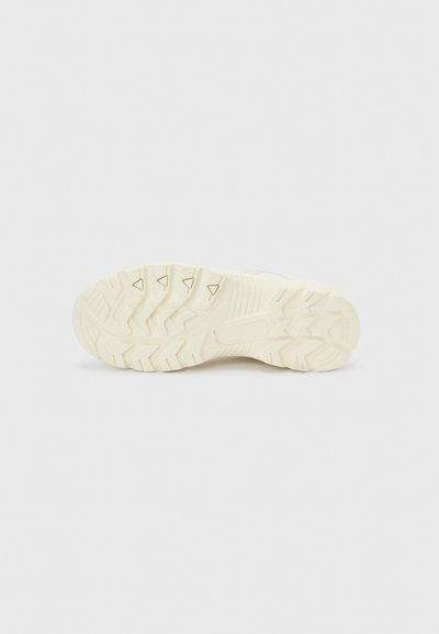 Σόλα ενός ανοιχτό μπεζ παπουτσιού με βαθιά ανάγλυφα και τριγωνικά σχέδια σε απλό λευκό φόντο.