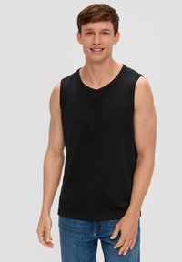 Zwarte mouwloze tanktop van katoen, met een ronde hals, schone randen, gedragen met blauwe spijkerbroek.