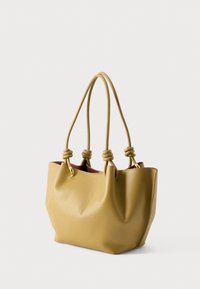 Žuta kožna torba s četiri uvezana ručkica i laganom teksturom, postavljena na jednobojnu bijelu pozadinu.