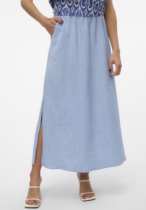 Jupe bleue longueur cheville avec fente latérale portée avec un haut bleu et blanc à motifs et des sandales blanches ouvertes à l'avant.