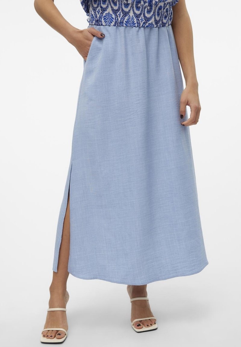 Jupe bleue longueur cheville avec fente latérale portée avec un haut bleu et blanc à motifs et des sandales blanches ouvertes à l'avant.
