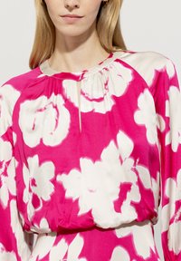 Blumenbluse in Rosa und Weiß, mit gerafftem Halsausschnitt, Schlüssellochdetail und locker sitzenden langen Ärmeln. Geschmeidige, seidenähnliche Textur.