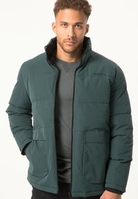Polstret grøn jakke med høj krave, med en frontlynlås og to store sidelommer. Stoffet har en glat, mat finish.