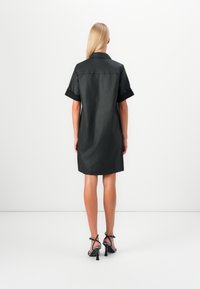 Abito camicia nero con maniche corte e colletto, dotato di una texture liscia, una vestibilità rilassata e un orlo che cade sopra il ginocchio.