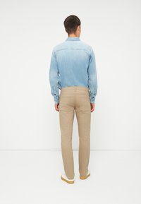 Lys denimskjorte med en falmet blå gradient, kombinert med khakibukser. Antrekket har et uformelt design med en strukturert passform og subtile sømmer.