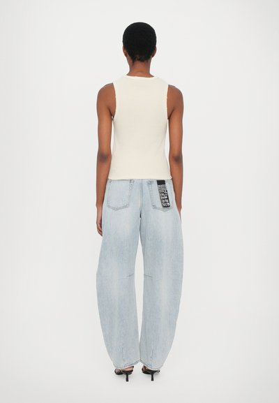 Geribbelde, crèmekleurige tanktop met brede bandjes, gecombineerd met lichtblauwe, losse spijkerbroeken met een zwart label op de achterzak. Hakken.