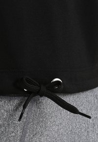 Svart bomullstopp med dragsko på nederkanten, med en silverfärgad ögla. Grått tyg synligt under.