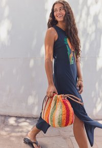 Tumesinine varrukateta kleit graafilise kujundusega, mis kujutab lõvi ja taimi. Kootud mitmevärviline kott punaste, oranžide ja roheliste triipudega. Mustad plätud.