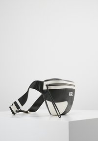 Musta-valkoinen vyölaukku, joka on valmistettu sileästä nahasta. Siinä on vetoketjullinen suljenta, säädettävä hihna ja kohokuvioitu "KARL"-logo edessä.