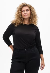 Svart långärmad topp i mjukt material, med rund halsringning och avslappnad passform, som matchas med svarta åtsittande byxor.