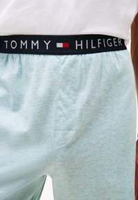 Világoskék pamut rövidnadrág fekete gumírozott derékkal, amelyen a "TOMMY HILFIGER" logó található, valamint egy oldalsó zseb részlet.