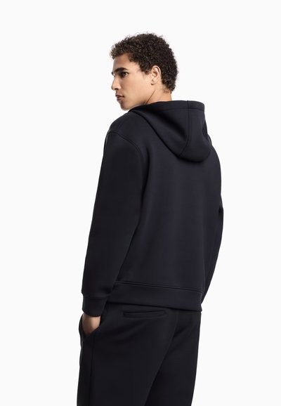 Sudadera con capucha negra de textura suave. Cuenta con un bolsillo frontal, un ajuste ligeramente holgado y puños y dobladillo acanalados.