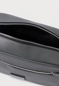 Saco de couro cinza-escuro com dois zíperes prateados, um parcialmente aberto mostrando um interior de tecido preto.