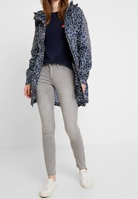 Navy raincoat with white star pattern, paired with gray skinny jeans and white sneakers. Jacket features a hood and zipper pockets.
