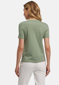 Korte mouwen groene t-shirt van zachte katoen. Klassiek ontwerp met ronde hals. Glad textuur zonder zichtbare patronen. Gedragen met lichtgekleurde broeken.