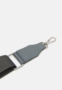 Grå læderrem med tekstureret overflade, sølvfarvet hardware og en sort vævet sektion, der har en clip i enden til fastgørelse.