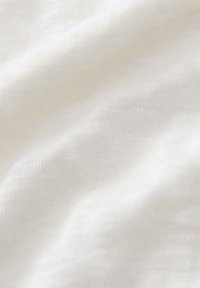 Tessuto bianco con una morbida trama a maglia testurizzata e leggere pieghe, che evidenziano le sue qualità leggere e traspiranti.