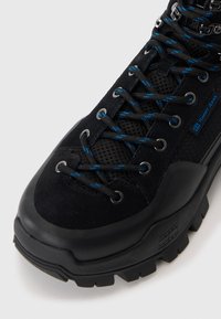 Black hiking shoe features a textured suede upper, mesh panels, blue and black laces, and a sturdy rubber sole with pronounced tread.