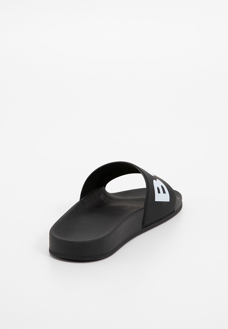 Sandale en caoutchouc noir avec un design ouvert, semelle intérieure texturée et grand logo blanc sur le côté. Semelle plate avec une finition lisse.