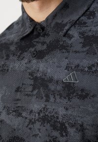 Polo tričko v černé a šedé barvě s texturovaným vzorem, s límečkem, dvěma knoflíky a malým logem na hrudi.