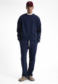 Sweatshirt bleu marine et pantalon de survêtement assorti en tissu doux. Le sweatshirt a un col rond et un ourlet côtelé, tandis que le pantalon possède un cordon de serrage.