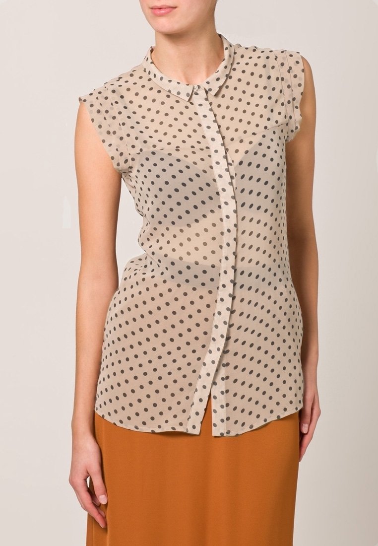 Blusa sin mangas de color beige con lunares, cierre frontal con botones, fabricada en tejido suave, con dobladillo curvado y cuello redondo.