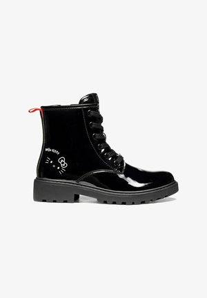 Botte de combat noire brillante à lacets avec semelle épaisse et petit motif blanc du visage de Hello Kitty près du talon et languette rouge à l’arrière.