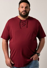 Burgundy kortärmad t-shirt i bomull med snörning i halsringningen och metalldetaljer. Avslappnad passform, mjuk textur och subtilt stretch.