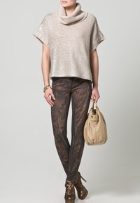 Ljust beige stickad tröja med krage, matchad med mörka, strukturerade skinnybyxor. Håller en beige handväska och bär bruna snörskor.