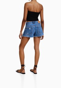 Shorts vaqueros de color azul claro con bordes deshilachados y un ligero desgaste, combinados con una camiseta negra ajustada y sandalias negras con tiras.