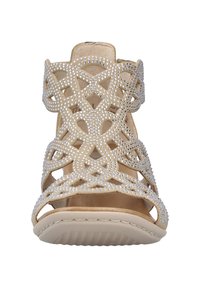 Sandale à talon beige présentant un design découpé élégant orné de strass, bout ouvert et bride de cheville pour un maintien sûr. Semelle plate.