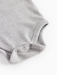 Pogled od blizu na sivo rebrasto dno otroške bodice s tremi pritiski na belem ozadju.