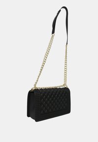 Borsa a mano nera trapuntata di forma rettangolare, con catena dorata e tracolla nera, superficie testurizzata con borchie lungo i bordi.