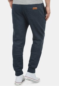 Dark blue sweatpants with a tapered fit, ribbed cuffs, and a rear pocket featuring a tan leather label. Worn with white sneakers.