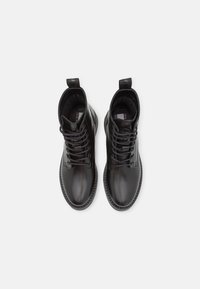 Botas de cuero negro hasta el tobillo con diseño de cordones, punta redondeada y suela cosida. Presenta un lazo en la parte posterior y un acabado suave.